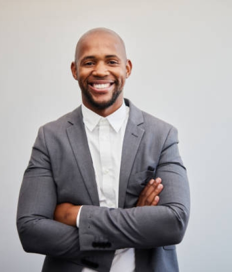 Portrait of a smiling young businessman wearing a suit standing with his arms crossed in front of a white wall in an office